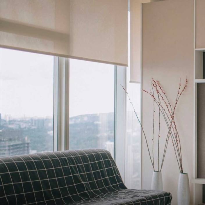 Cortinas enrollables en tela translúcida color crema colocadas en ventanal con nista a la ciudad